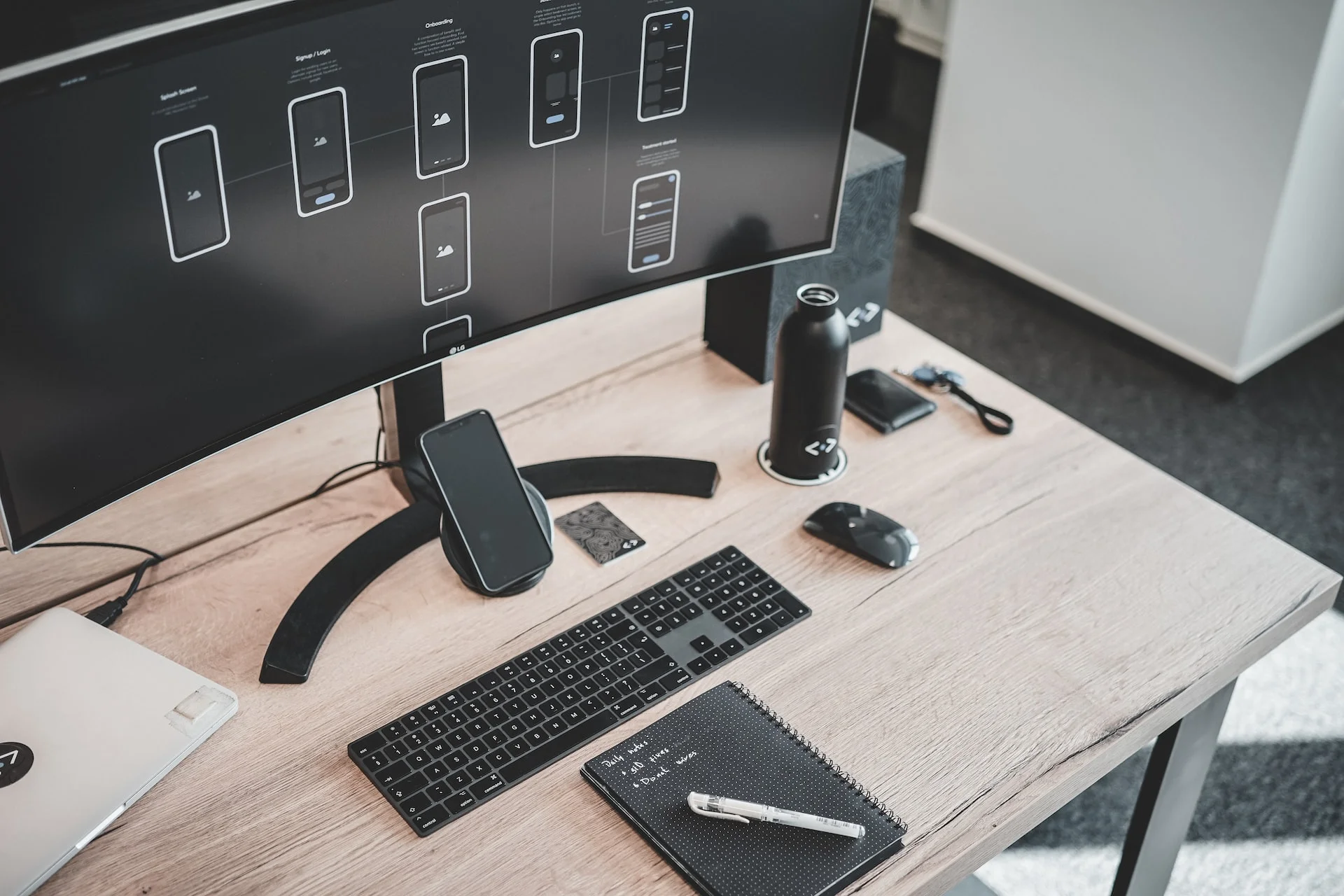 A designer's desk with mobile app wireframes displayed on a curved monitor